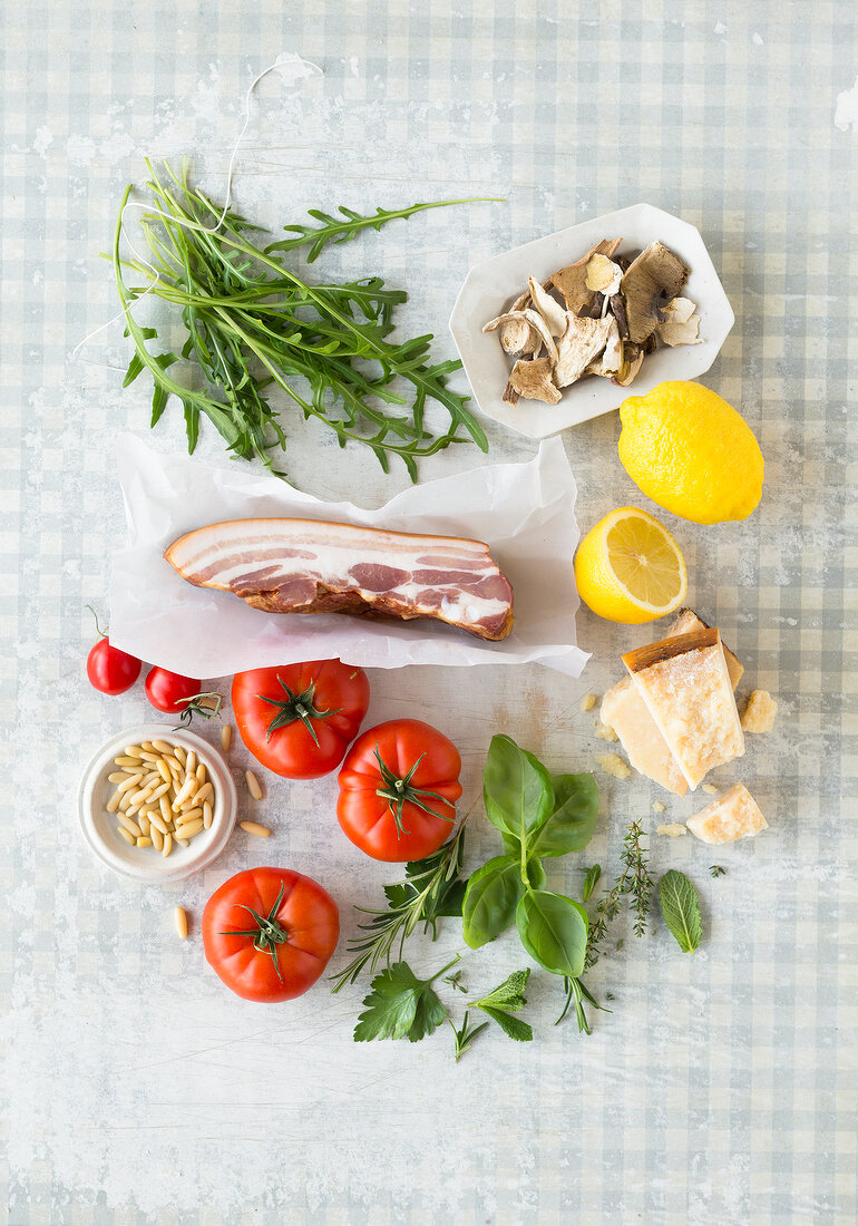 Fresh herbs, tomatoes, parmesan cheese, mushrooms and bacon on chopping board