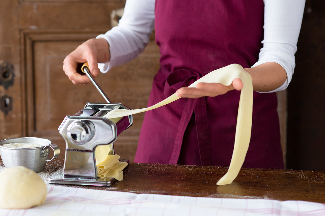 Woman making homemade noodles with pasta machine on table