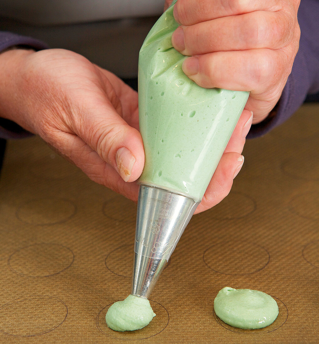 Close-up of hands making macarons through piping bag on baking paper