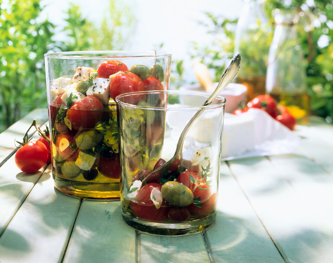 Glass with olives, vine tomatoes and feta cheese in olive oil on wooden table