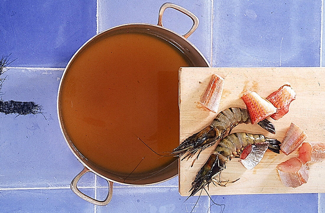 Topf von oben auf blauen Kacheln, darüber ein Holzbrett mit Fisch