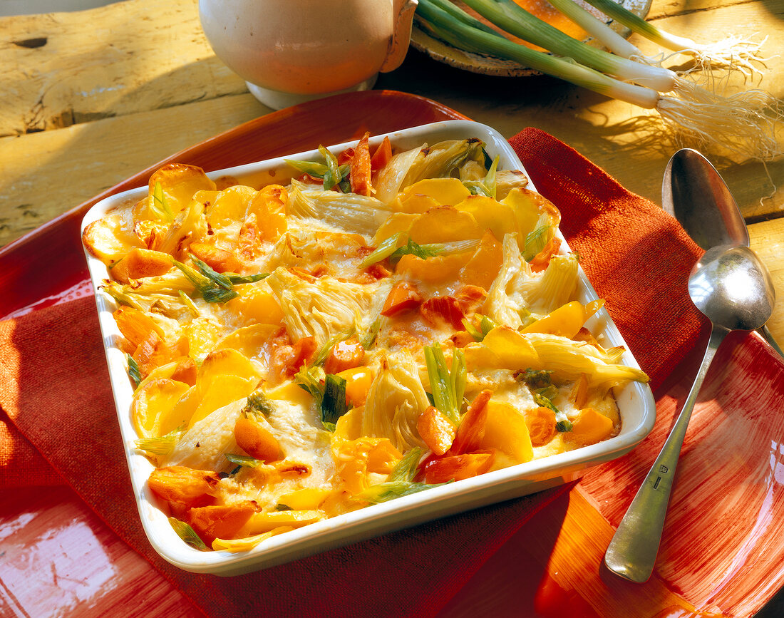 Vegetable gratin with feta cheese, fennel, carrots, potatoes and peppers on square plate