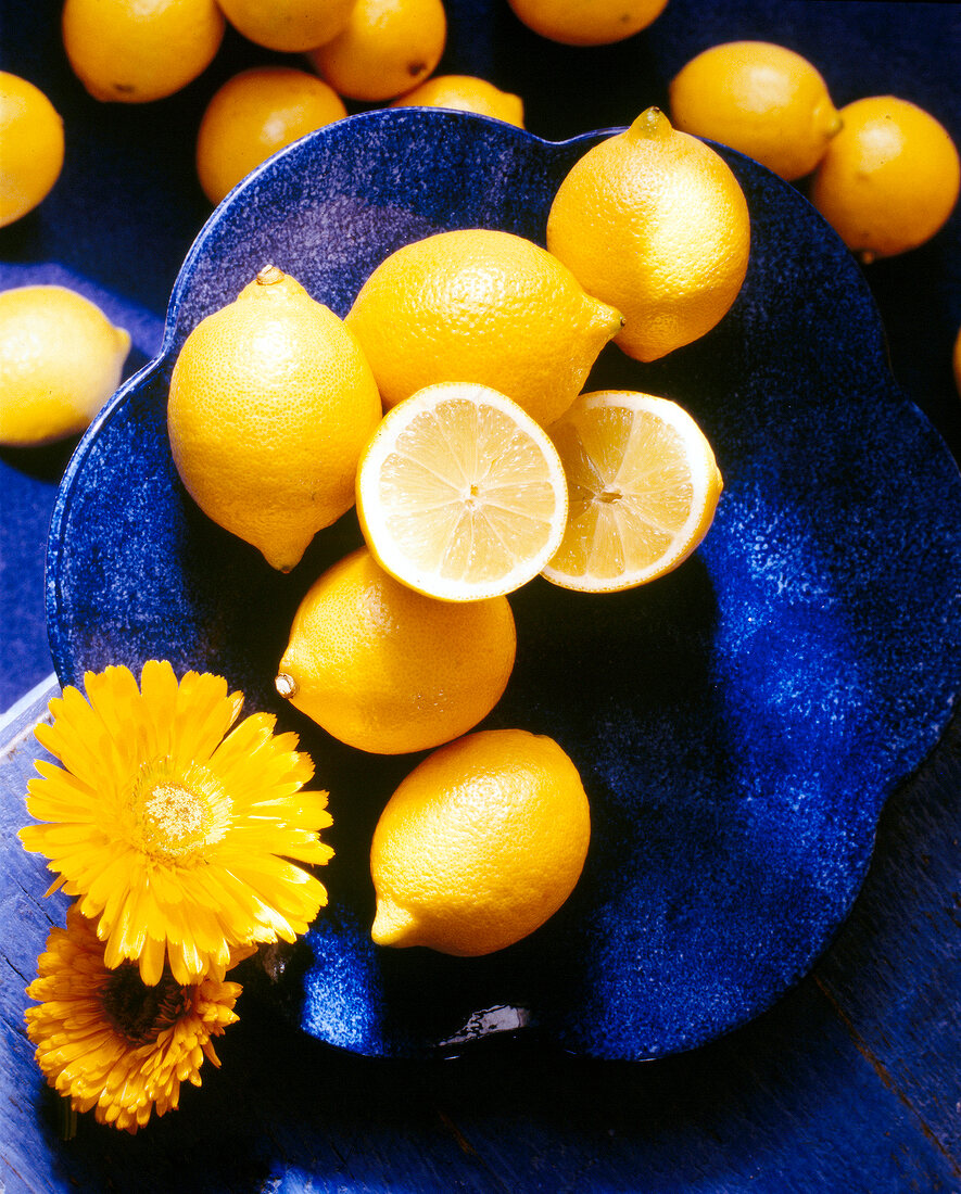 Whole and halved lemons with marigold flowers on blue plate