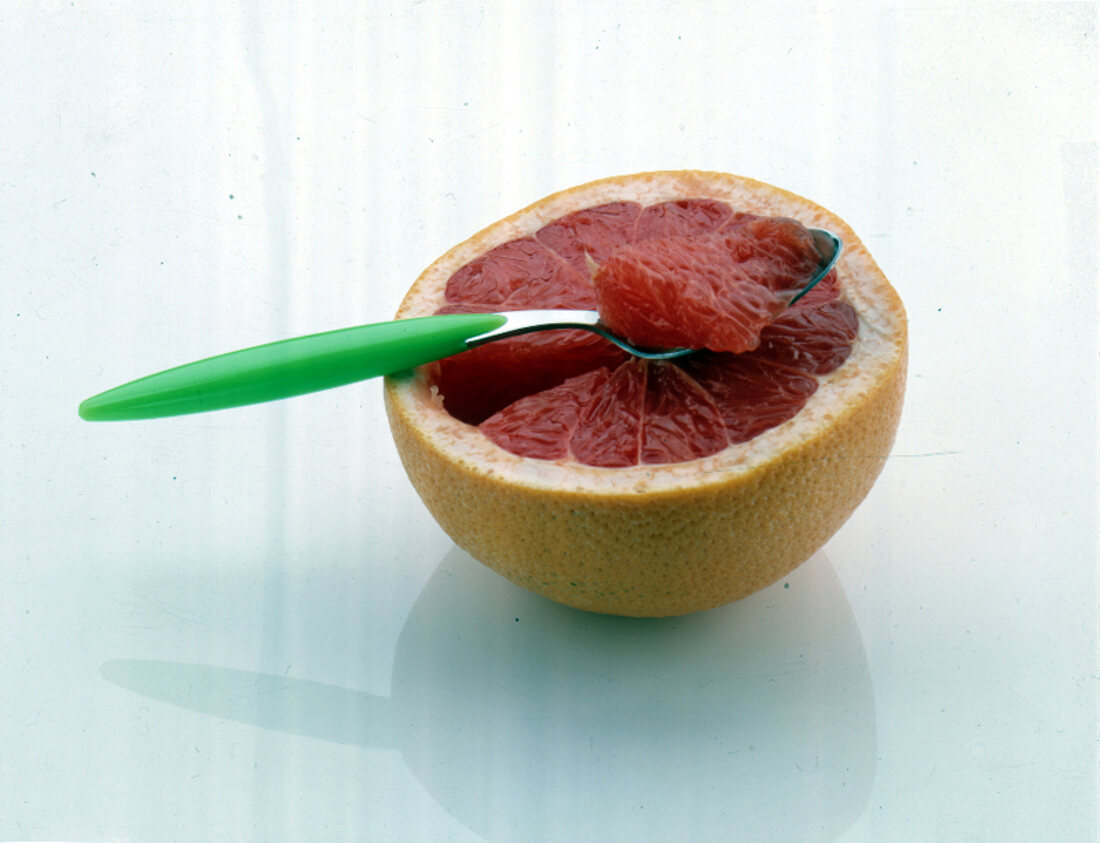 Eine halbe Grapefruit mit Löffel freigestellt