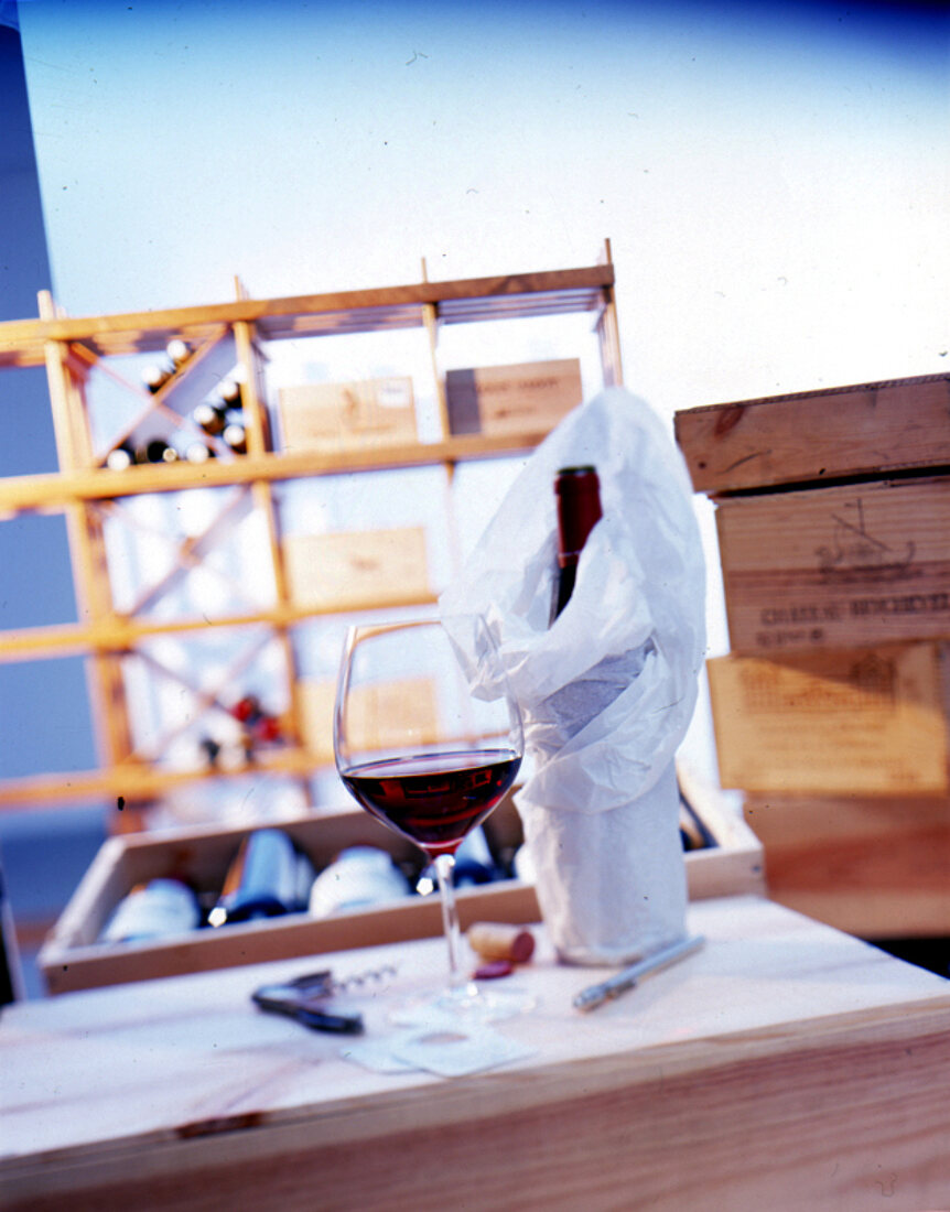 Rotwein in einem Glas, in Papier eingewickelte Flasche