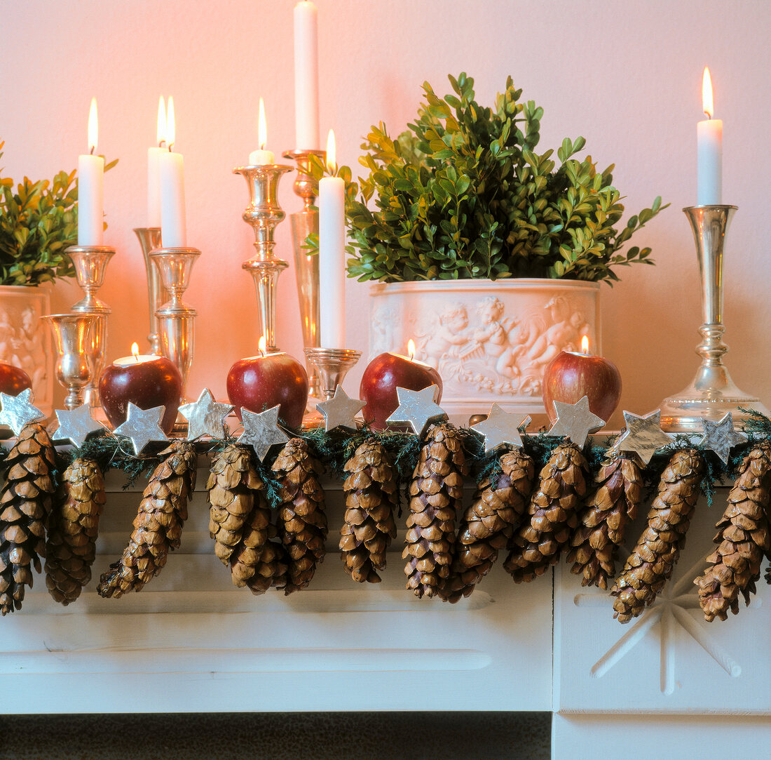 Mantelpiece decorated with pine cones, apple and candles for Christmas