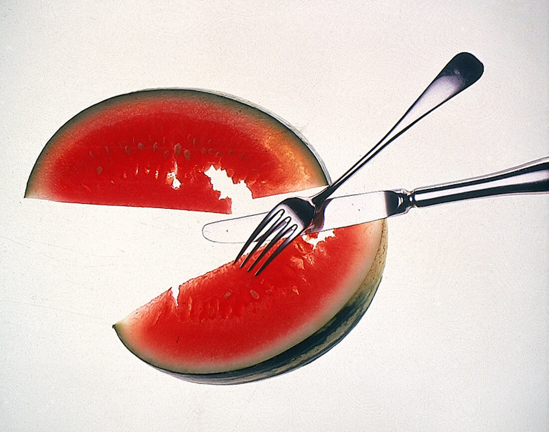 Zwei Scheiben einer Wassermelone mit Messer und Gabel