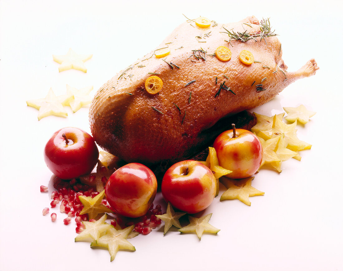 Roast goose with fruits and herbs on white background