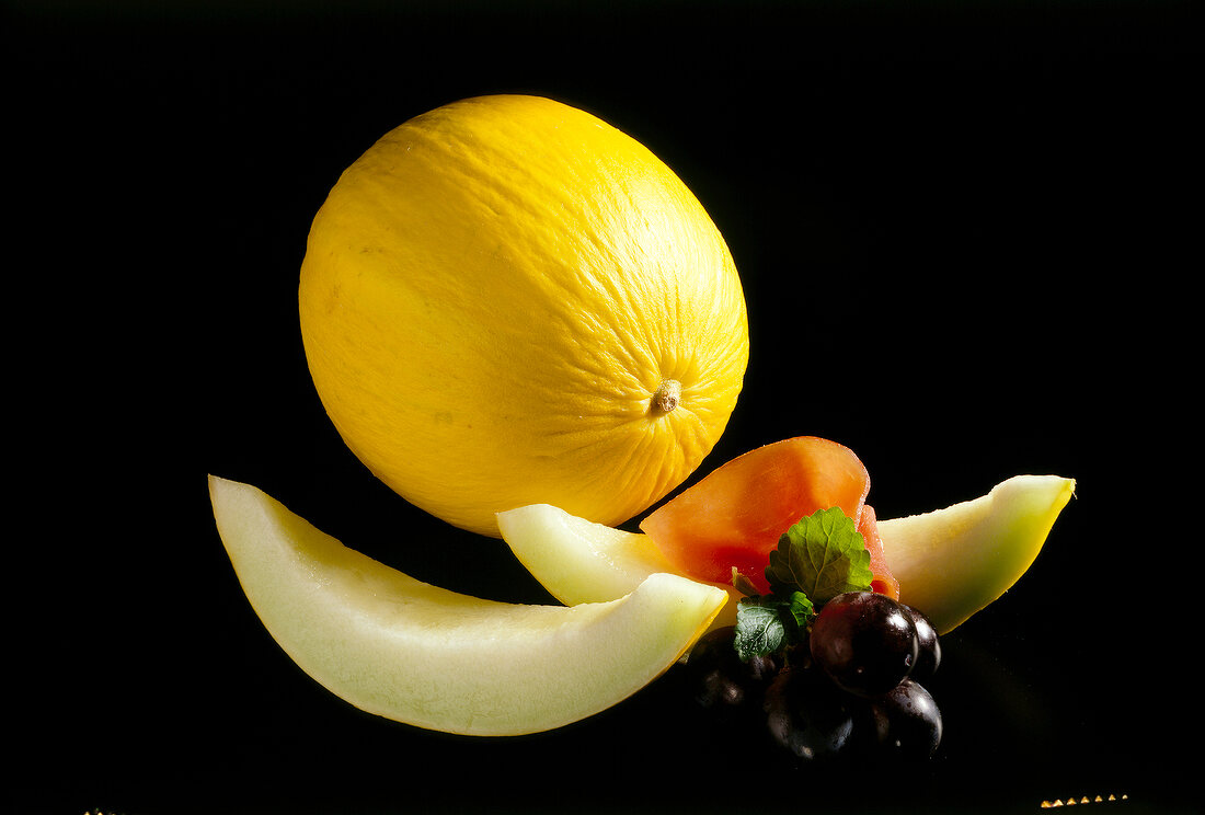 Whole cantaloupe with two slices on black background