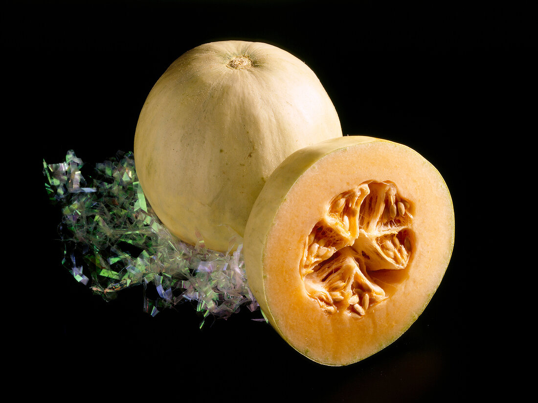 Close-up of whole and halved cantaloupe melons on black background