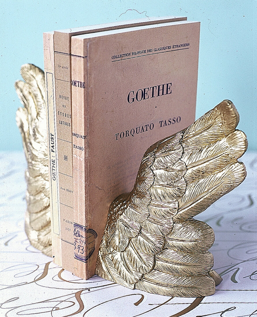 Buchstützen in Form von goldenen Engelsflügeln, dazwischen Schreibhefte