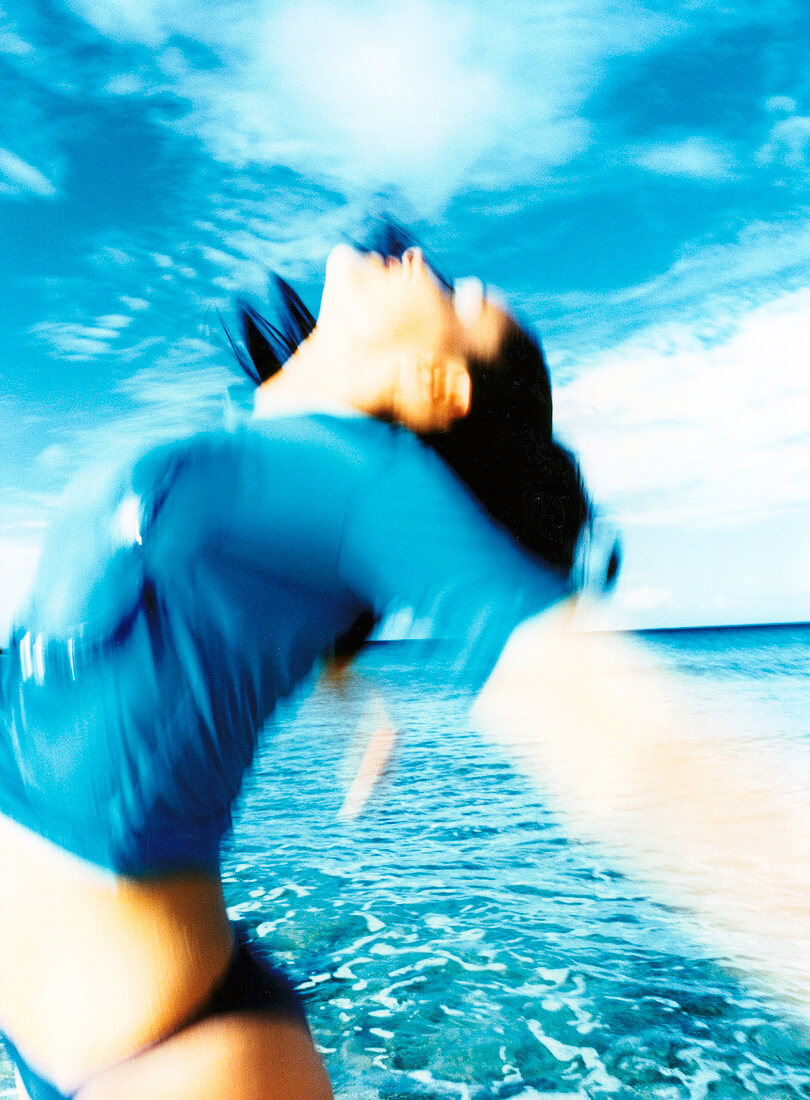 Side view of woman wearing blue t-shirt, jumping in air on beach