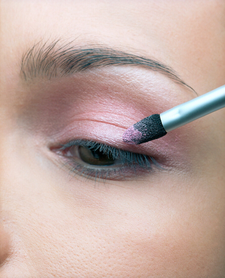 Extreme close-up of woman's eye while applying pink eye shadow