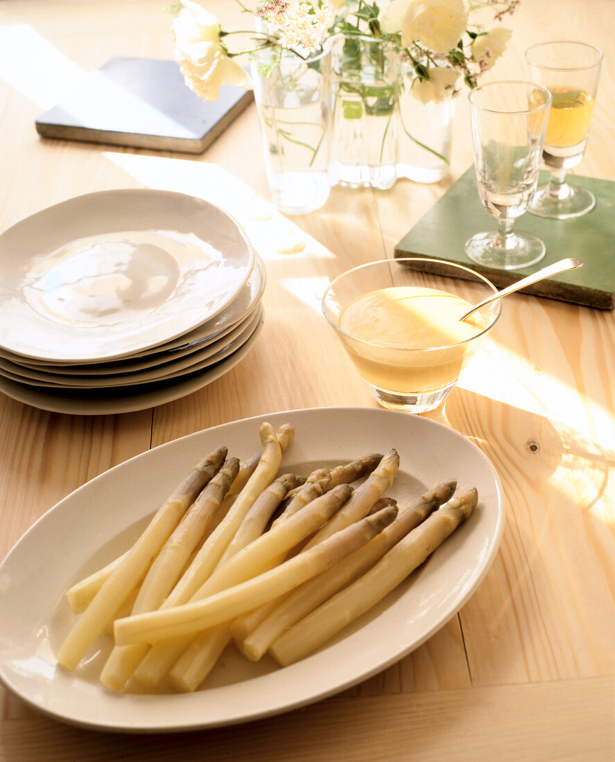 Cooked asparagus in plate with bowl of sauce on table