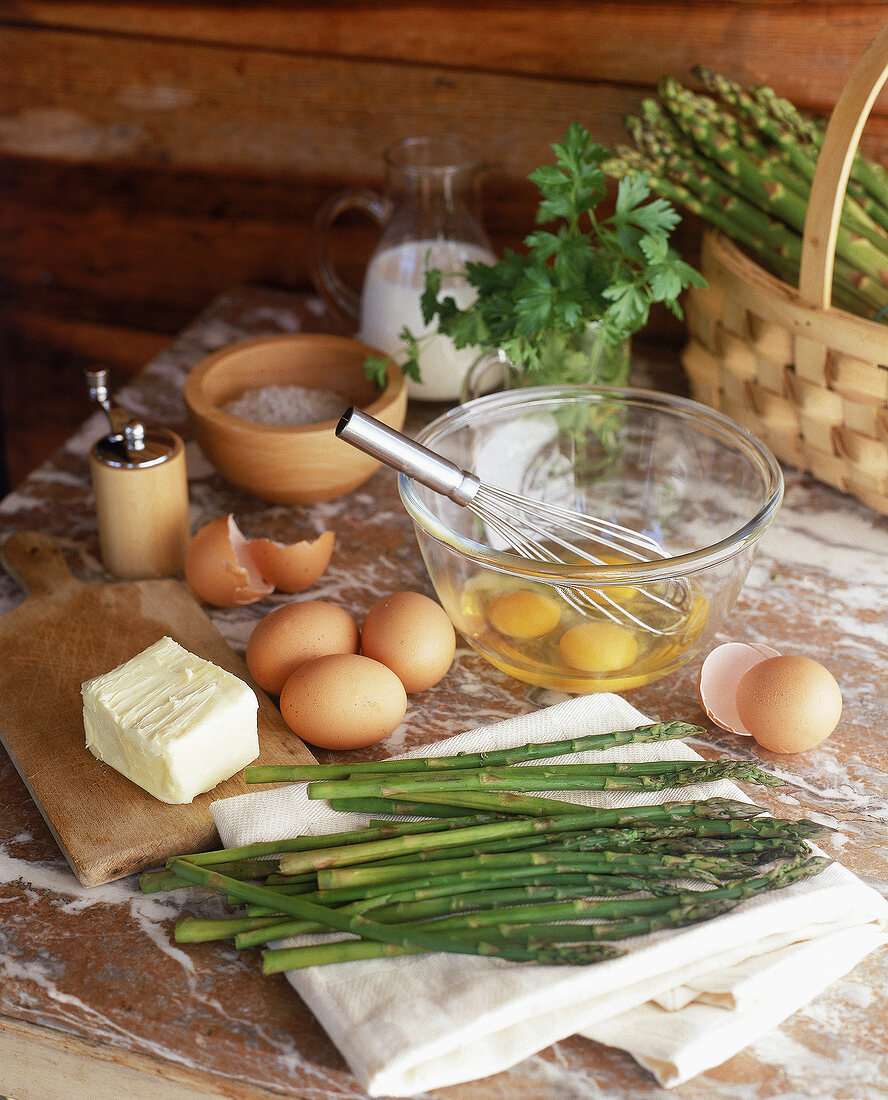 Roher gruener Spargel auf einem Handtuch,dahinter Eier + Butter