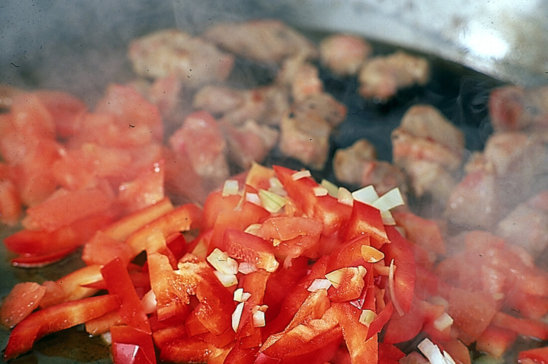 Schnitzelfleisch wird mit Paprikastreifen und Tomaten angebraten