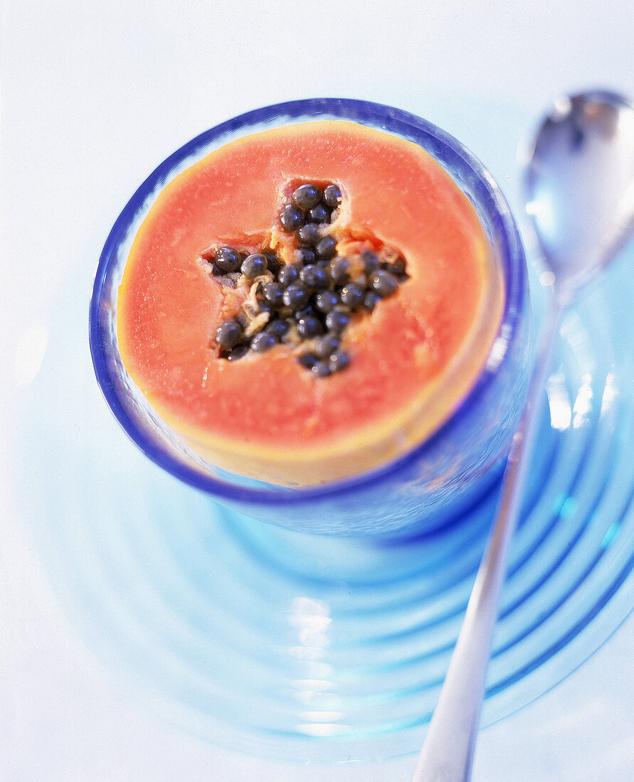 Halbierte Papaya mit Kernen in einem blauen Glas