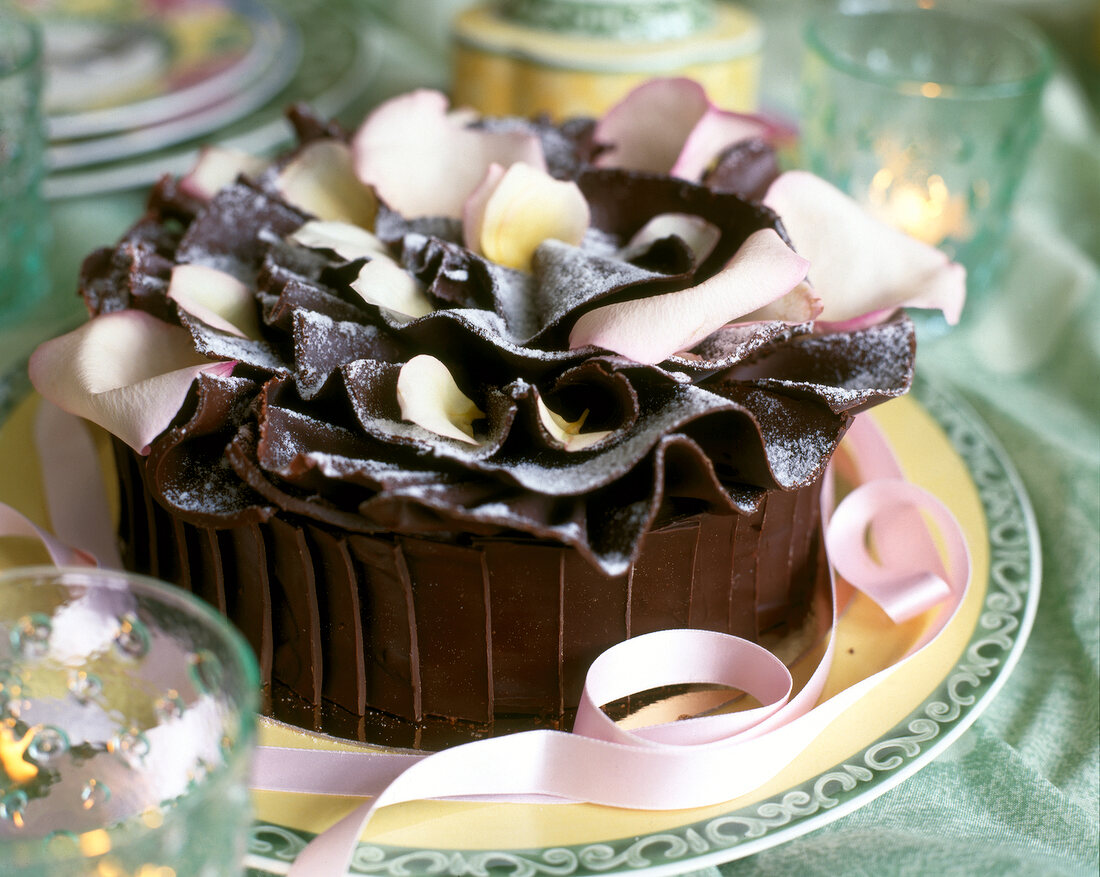 Chocolate charlotte cake with pink rose petals decorated with ribbons, close-up