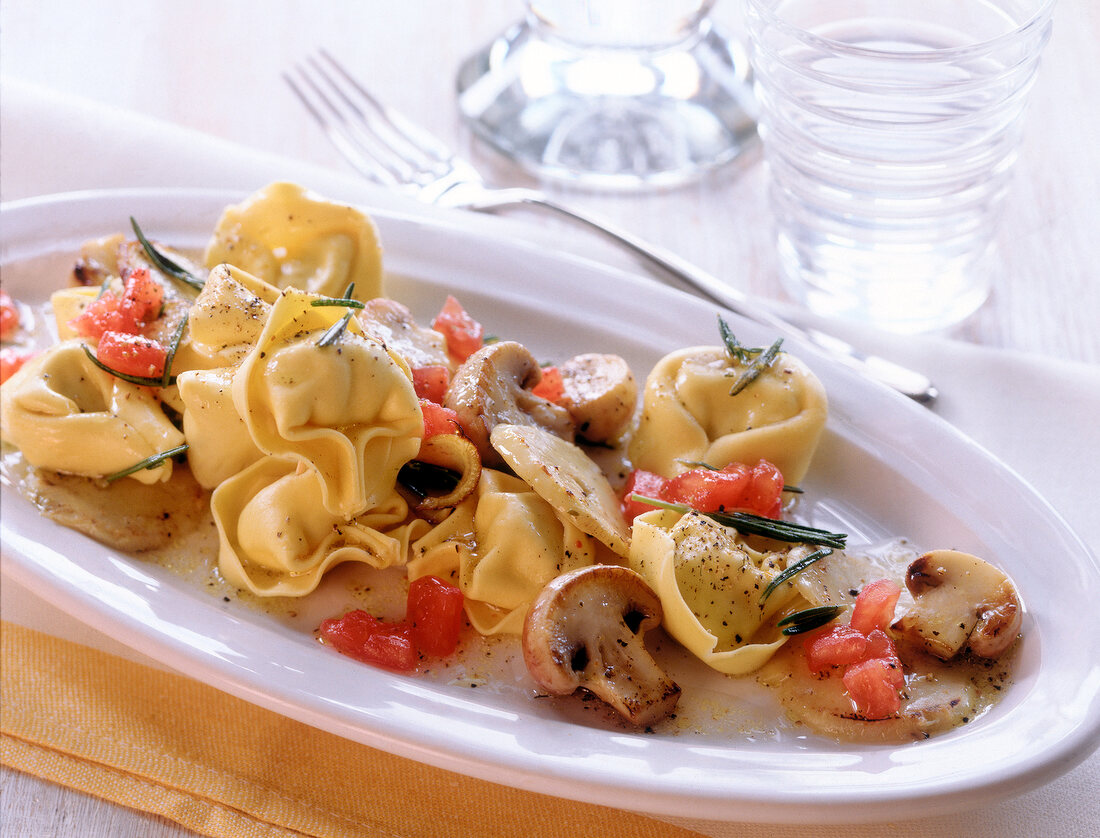 Tortellini with fried mushrooms and artichokes on oval plate