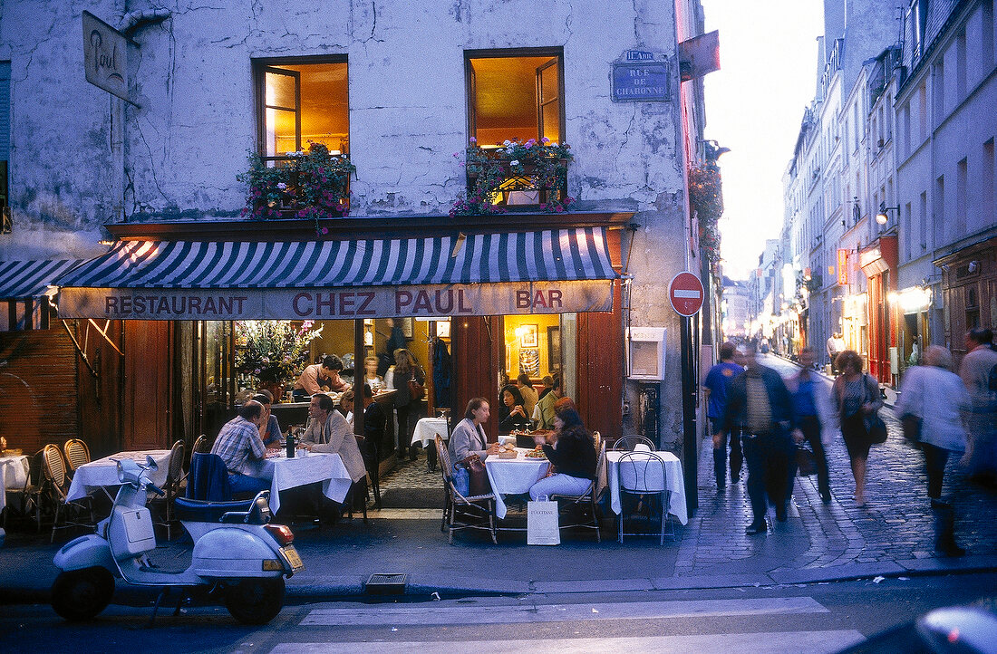 Front view of bistro Chez Paul with people and tables on street in evening