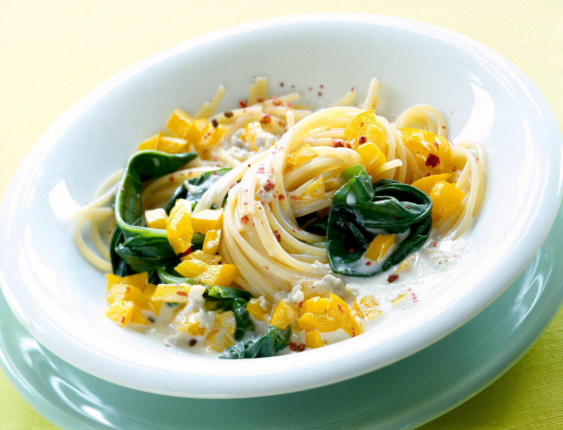 Spaghetti with yellow peppers, spinach and gorgonzola cheese in bowl