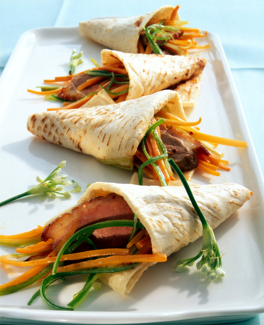Four tortillas stuffed with vegetables and duck meat on plate