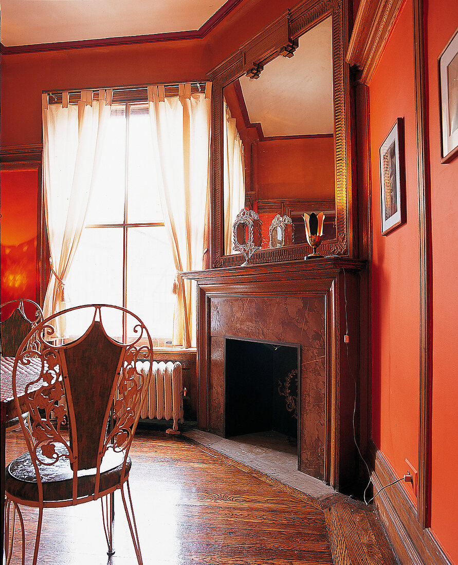 Zimmer mit Kamin u. Boden in dunklem Holz, rote Wände, Spiegel