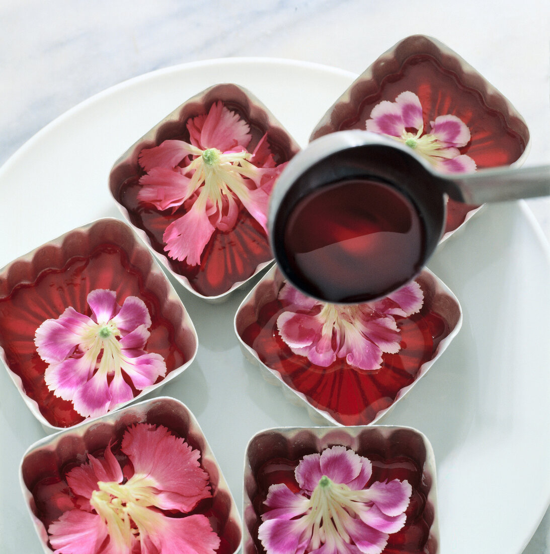 Rhubarb jelly being poured in jelly moulds with flowers on plate