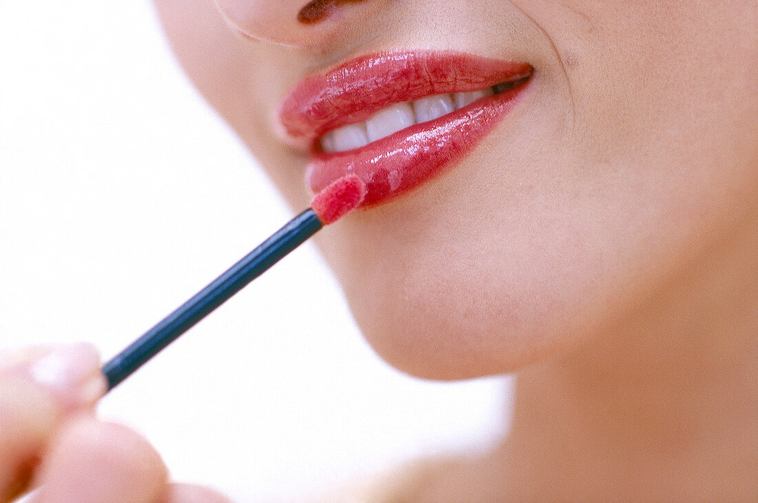 Close-up of woman applying red lip gloss with intense shine on, smiling