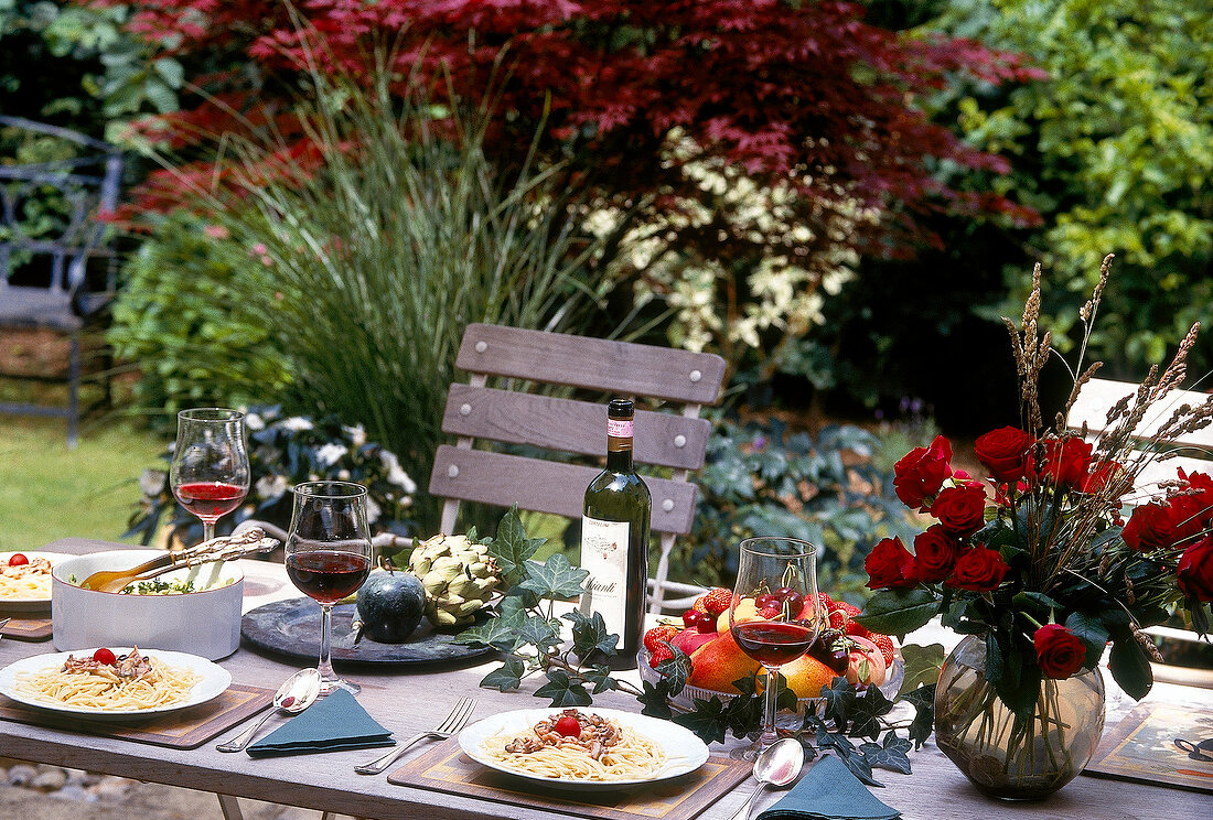 Gedeckter Tisch mit roten Rosen,Obst Rotwein und Spaghettigericht.