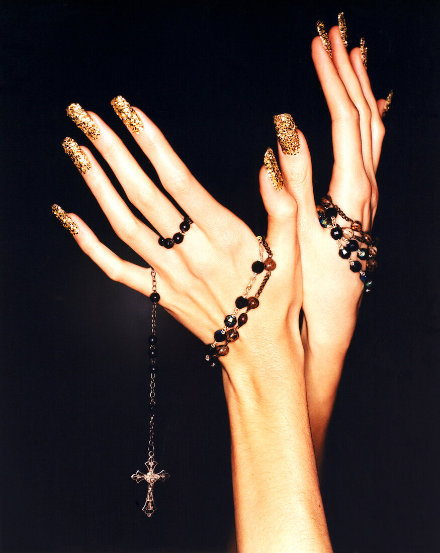 Close-up of woman's hand wearing colourful nail polish holding rosary