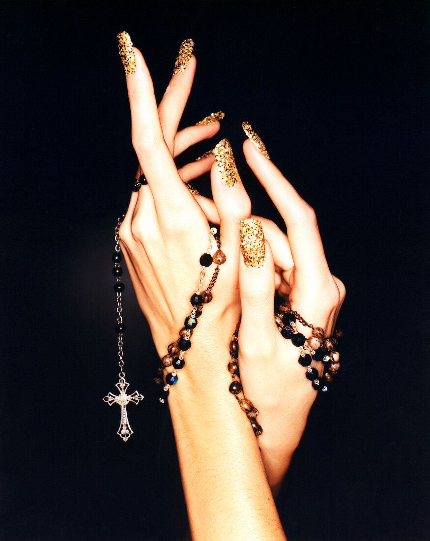 Close-up of woman's hand wearing colourful nail polish holding rosary