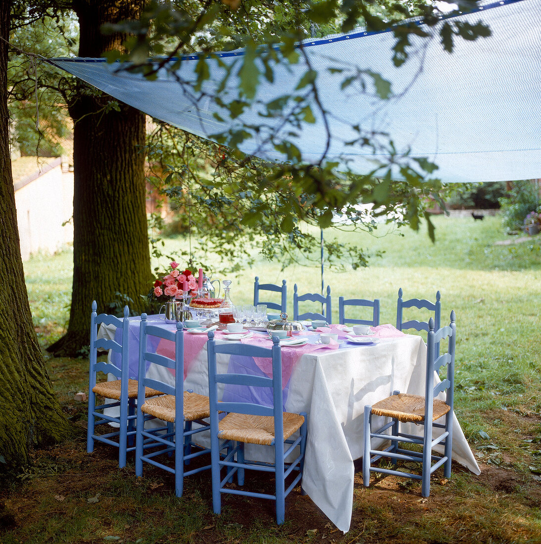 Eight blue chair around table under awning in garden