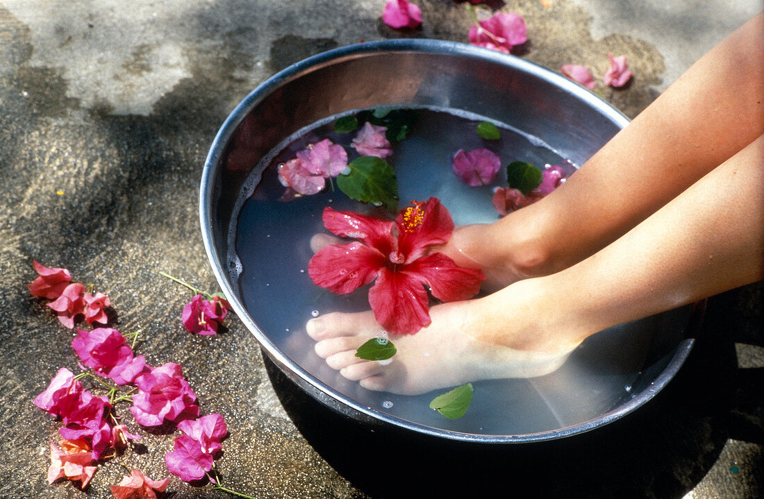 Frauenfüße in einem Fußbad mit Blüten