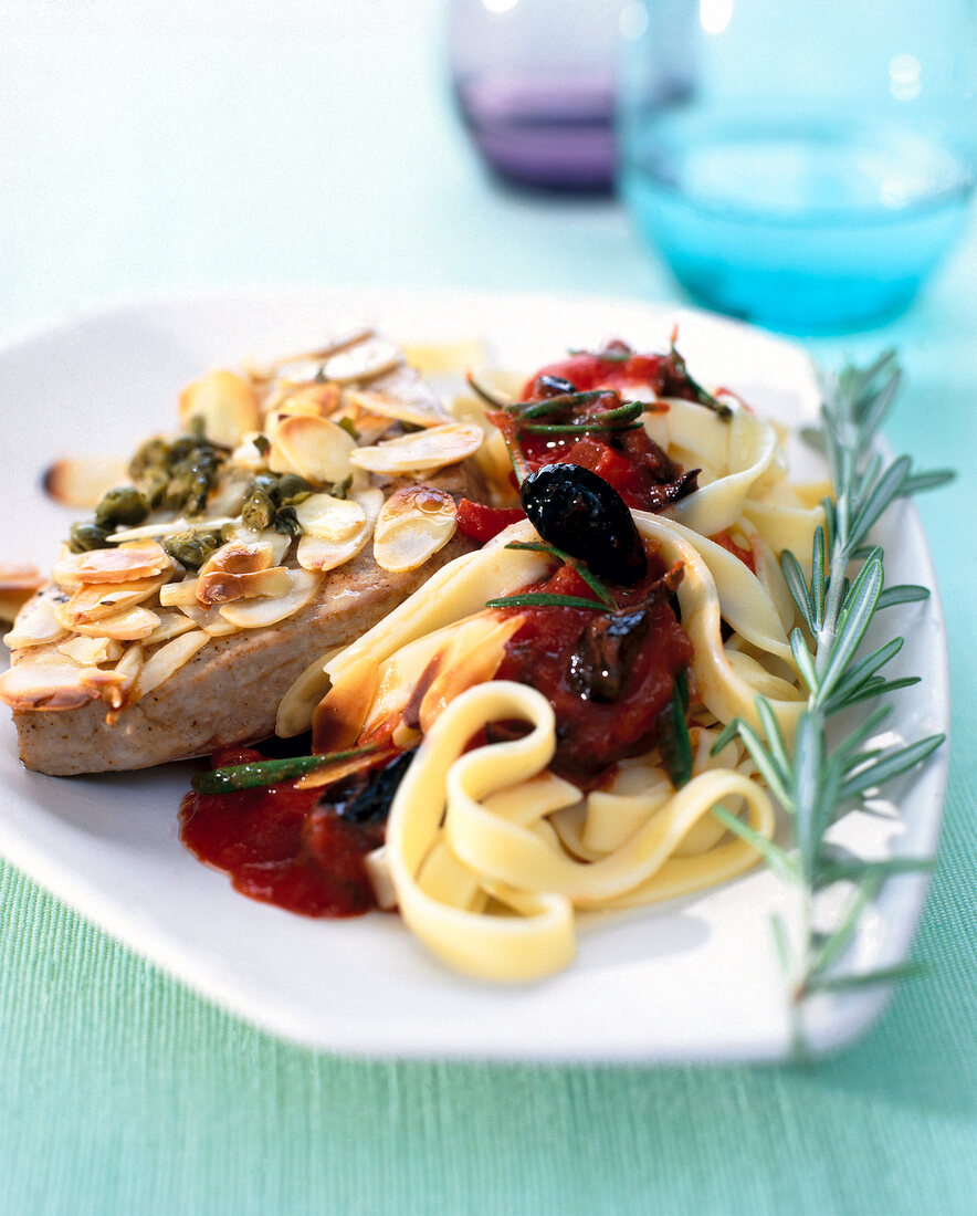 Close-up of tagliatelle with tomato sauce, tuna, olives, almonds and rosemary on plate