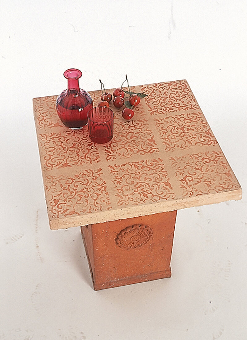 Kl Tisch mit Terrakottafuß,obendrauf Kirschen,rote Karaffe+rotes Glas.X