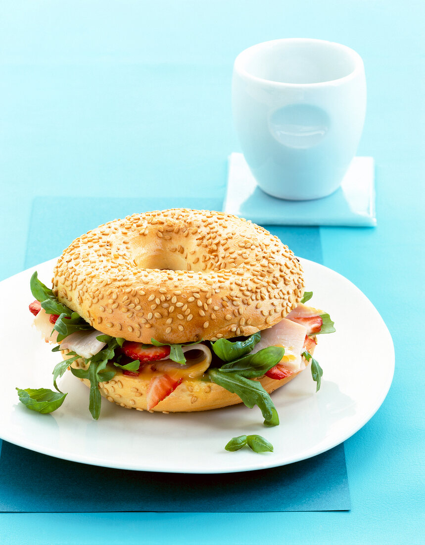 Sesame bagel with arugula, turkey breast and strawberries on plate