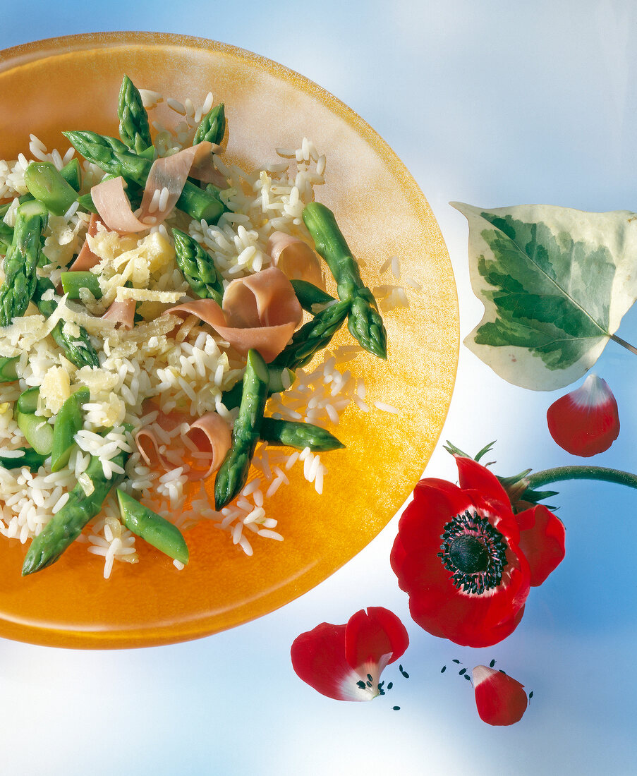 Rice with green asparagus and sliced ham on yellow plate