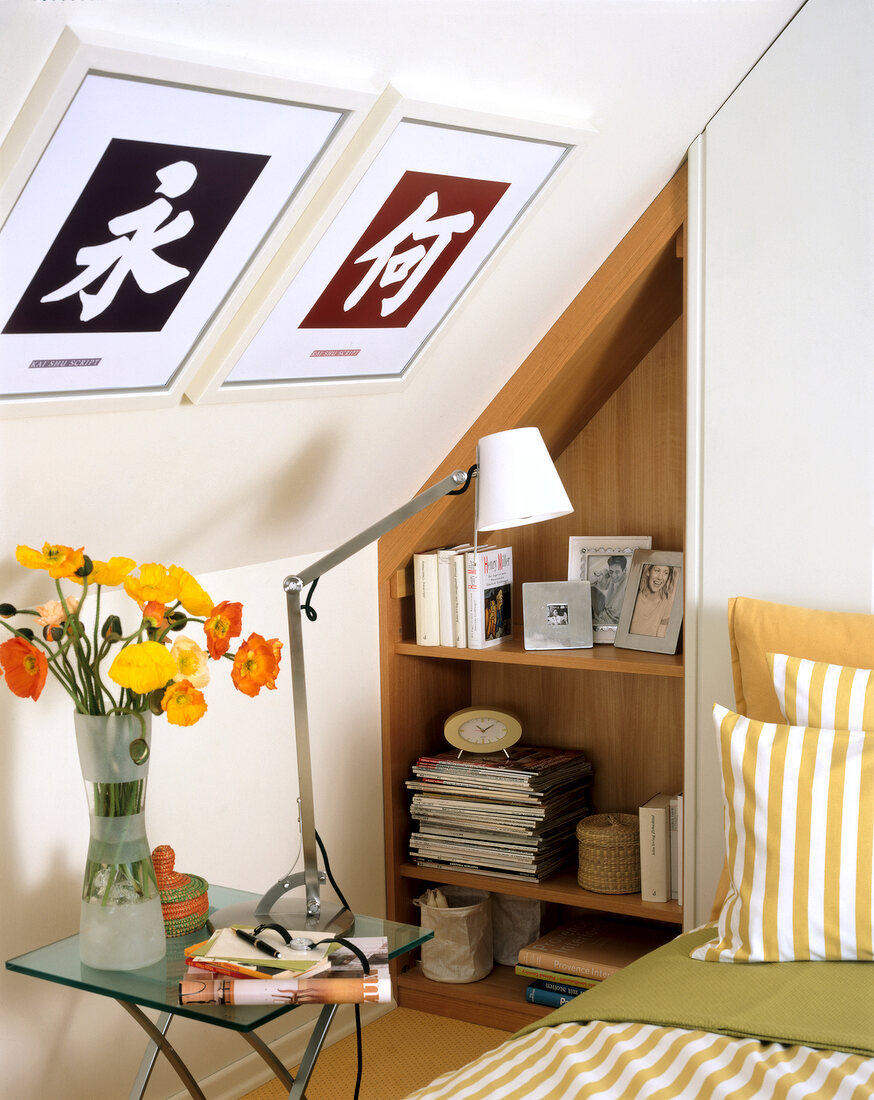 Glass table with vase of poppy flowers, lamp, built-shelf and bed in attic