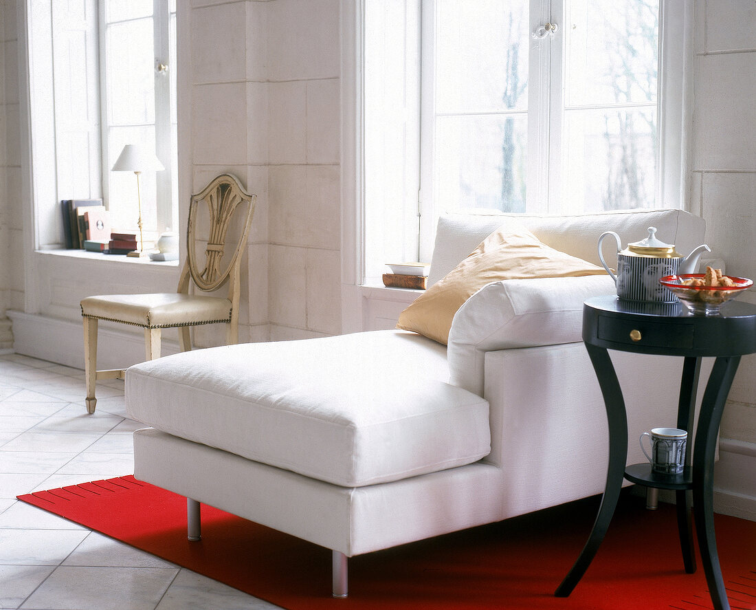 weiße Chaiselongue auf rotem Teppich kleiner Holztisch mit Schublade