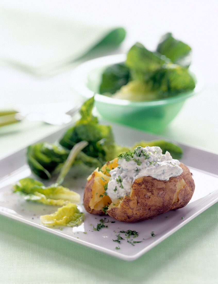 Baked potato with sour cream and herbs on white square plate