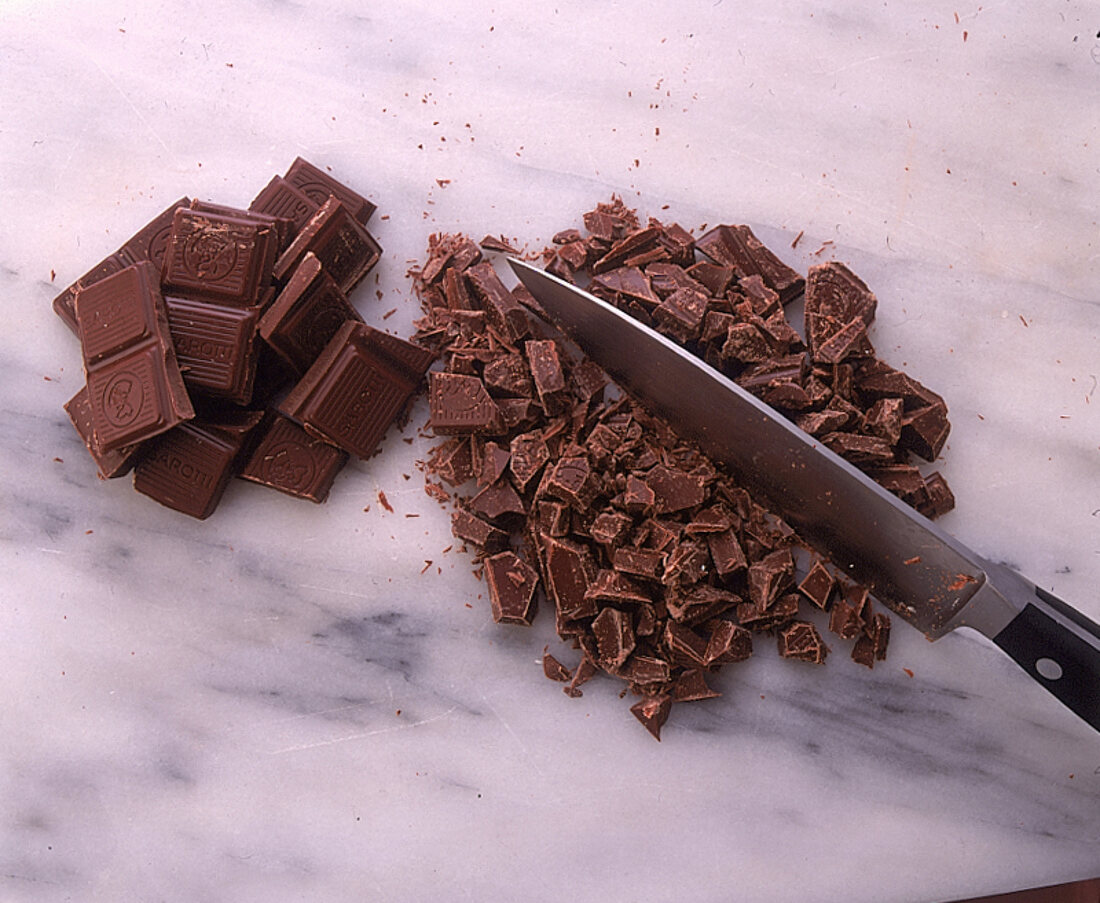 Mit großem Messer Schokolade in kleine Stücken hacken