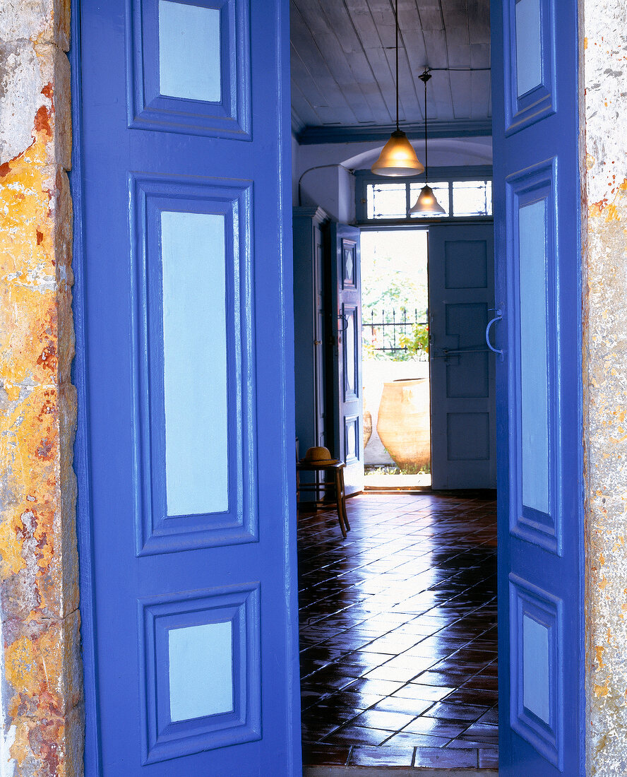 View of tiled hall and old water barrel through open wooden door