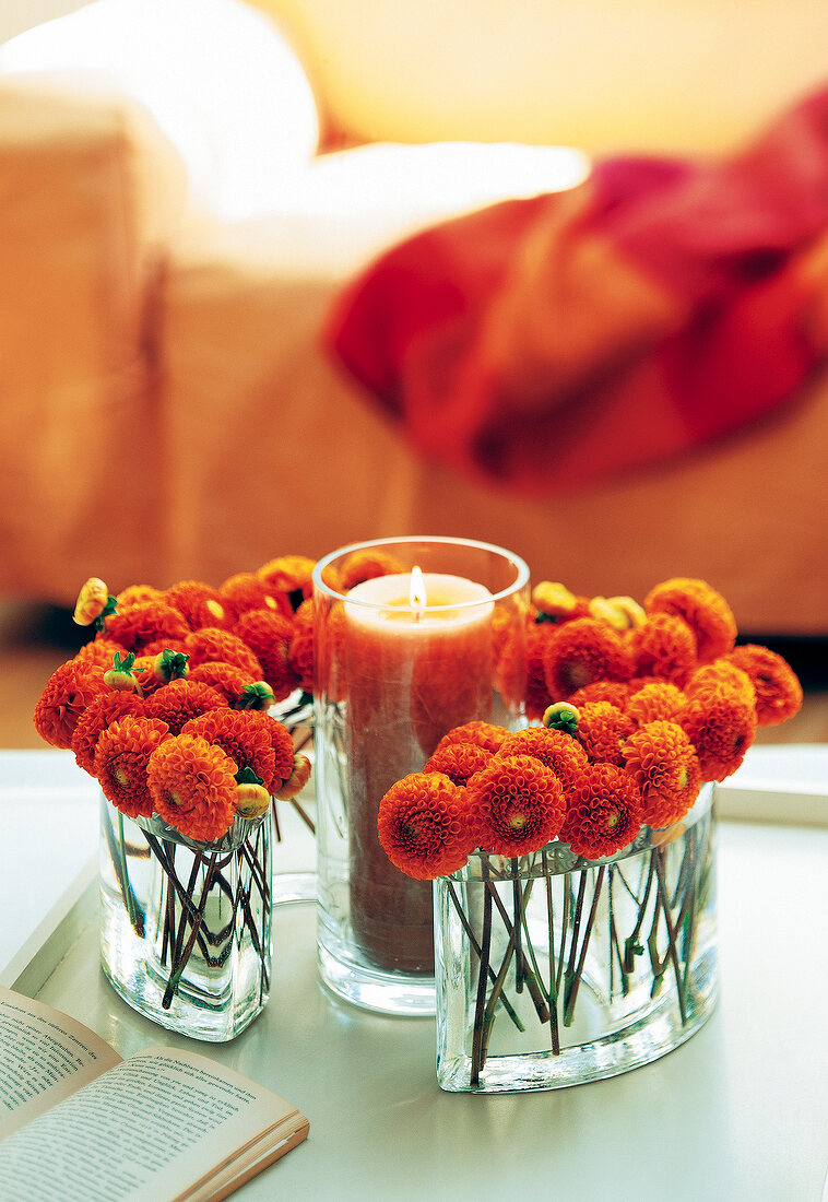 Glass of lit candle and flowers in vase on table