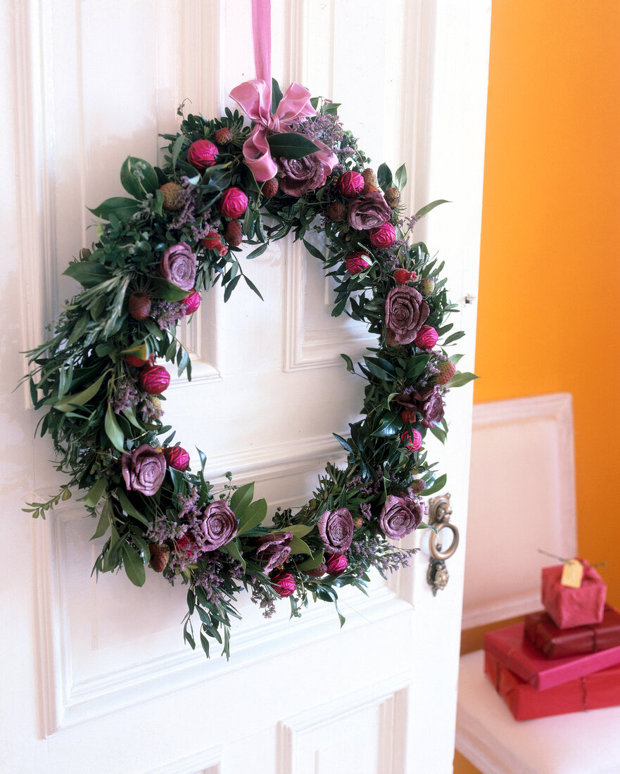 Wreath decorated with herbs and plastic roses hanging on door