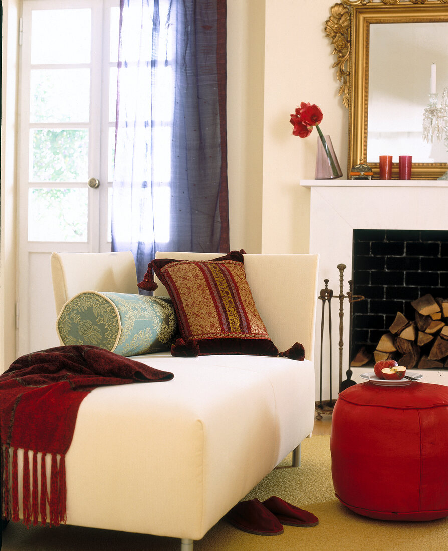 Cushions on long chair with red pouf in front of fireplace