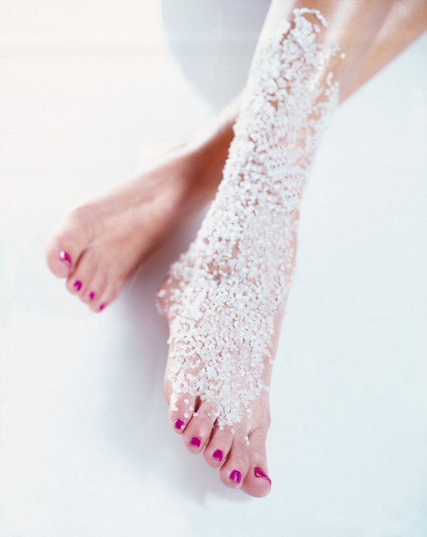 Close-up of woman's leg with pink nail paint and sea salt scrubbed on one leg