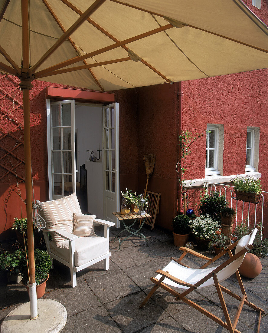 Terrasse mit großem Sonnenschirm, zwei Stühlen, rote Hauswand