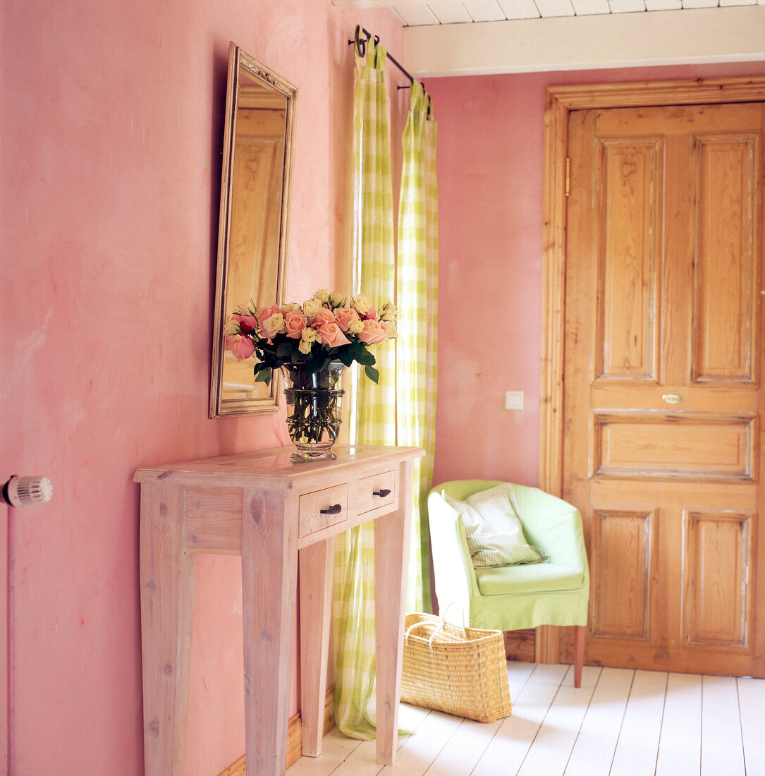 Console table with roses in vase and light green easy chair in corner of room