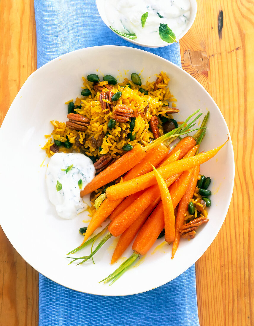 Oriental rice with pecans, pistachios, curry carrots and yogurt on plate